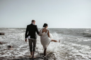bride and groom walk into sea in wedding gown and suit
